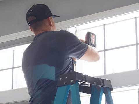 A man standing on a ladder installing window fixtures